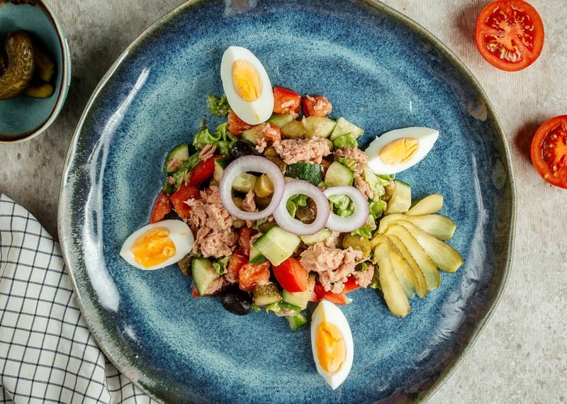 zdjęcie bezglutenowej sałatki z tuńczykiem, jajkiem i warzywami na niebieskim glinianym talerzu ustawionym na stole kuchennym