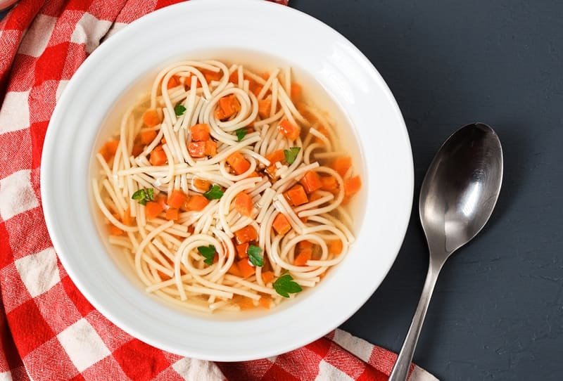Makaron bezglutenowy do rosołu w klarownym bulionie z warzywami, podany w białej misce – domowy makaron bez glutenu