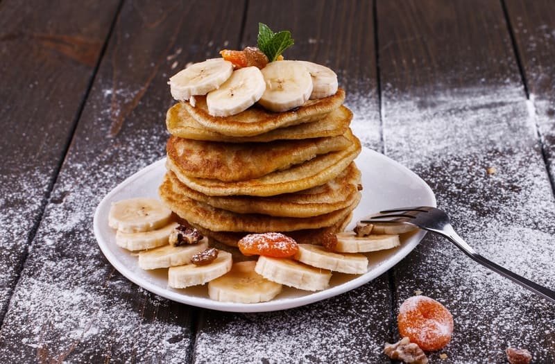 Fit placuszki z serka wiejskiego i banana bez mąki, puszyste i złociste, podane z bananem i suszonymi owocami na talerzu, naturalne światło, domowe otoczenie