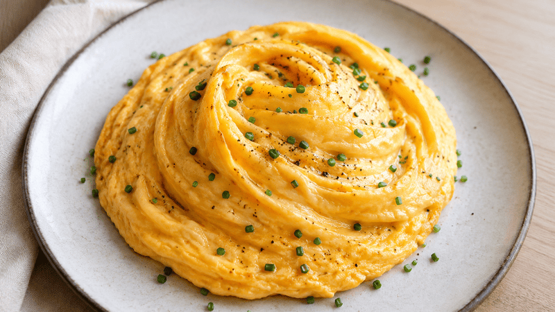 Puszysty omlet huragan o wirującej strukturze i kremowym środku podany na talerzu z posypką ze szczypiorku.
