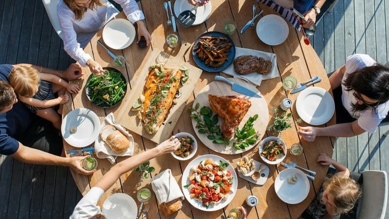 Goście przy restauracyjnym stole GF z rybą, mięsem, sałatkami i dodatkami